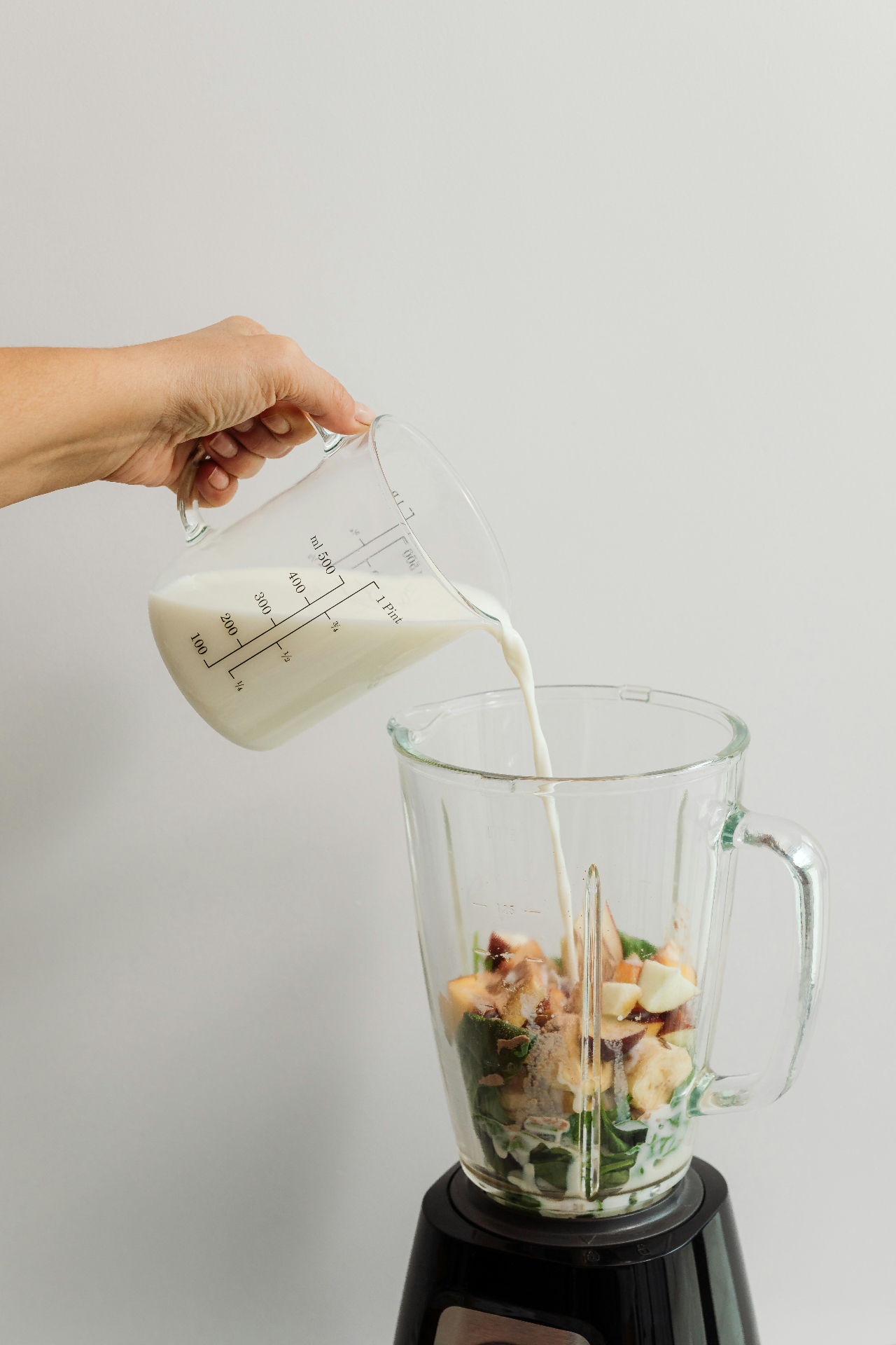 pouring milk into a blender of fruit and greens