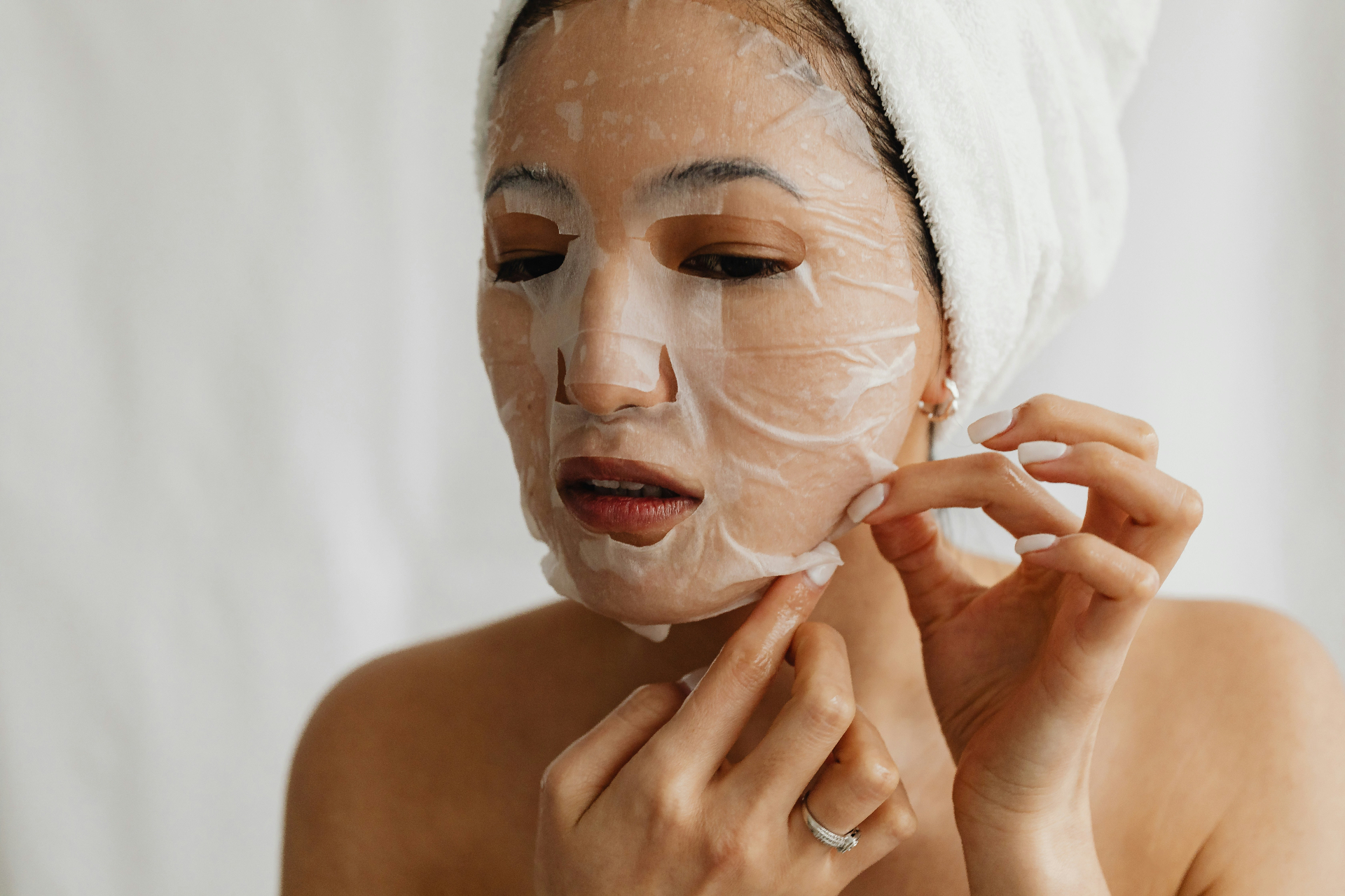 woman applying a sheet mask in a soft white robe